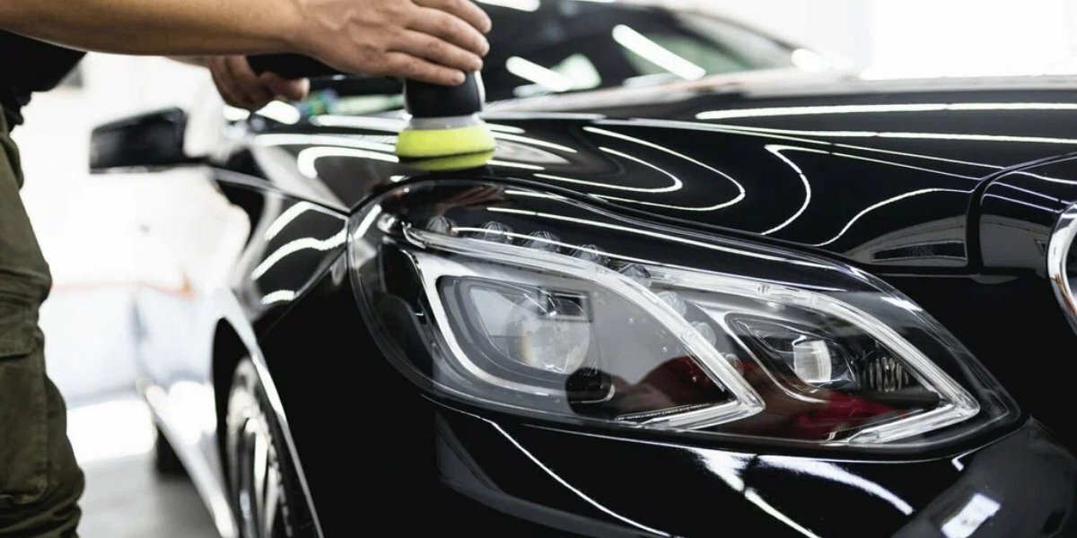 Professional technicians in black uniforms detailing a Rolls-Royce in a specialized cabin